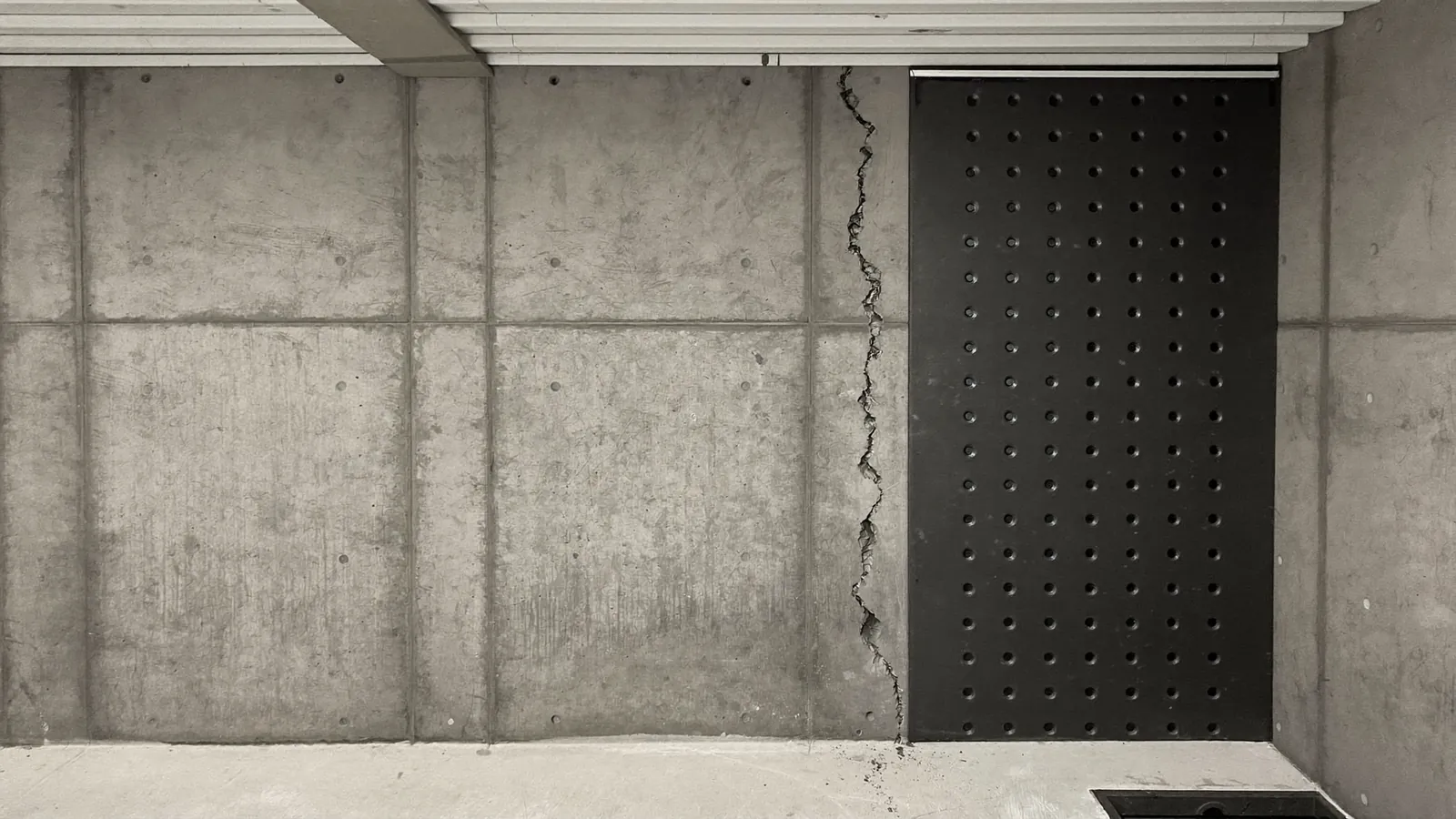 Interior basement wall with a sealed vertical crack and a drainage membrane fitted along the base, sump basin visible in the corner