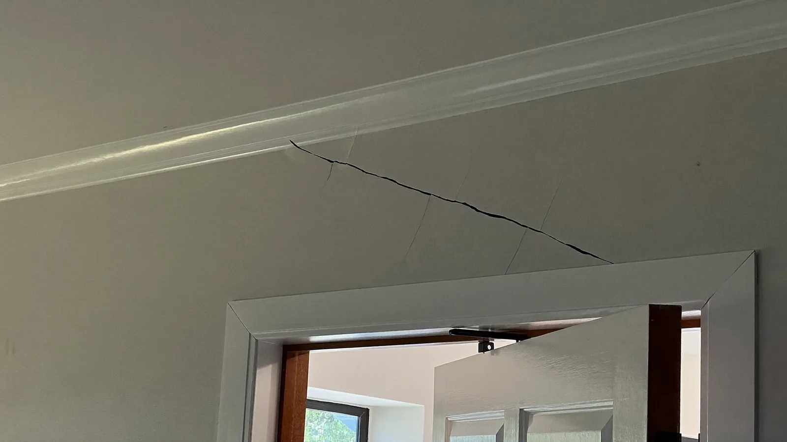 Diagonal drywall crack running from the top corner of an interior door frame, the door hung slightly out of square in its jamb