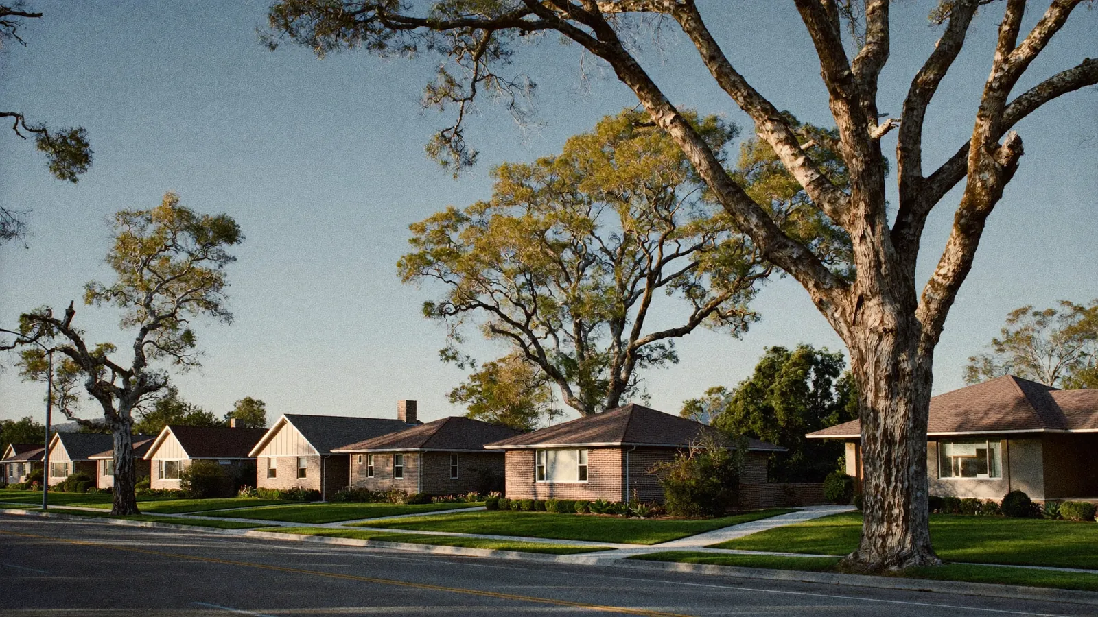Residential street in Edmond, Oklahoma lined with single-story red brick homes on wide lots, Cross Timbers blackjack oaks along the verge under a big prairie sky