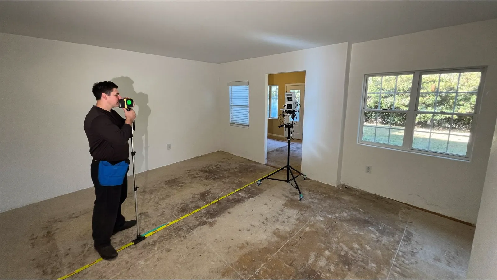 Technician taking a floor elevation reading with a rotating laser level and receiver in the empty living room of a slab-on-grade house