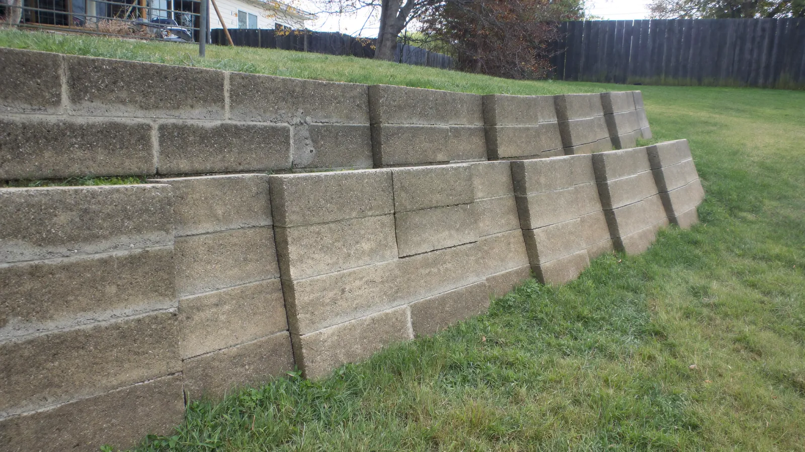 Segmental block retaining wall tilting outward at the top where saturated clay has pushed against it, behind an Oklahoma back yard